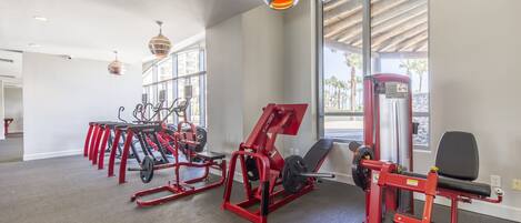 A gym with red exercise equipment, large windows, and hanging pendant lights.