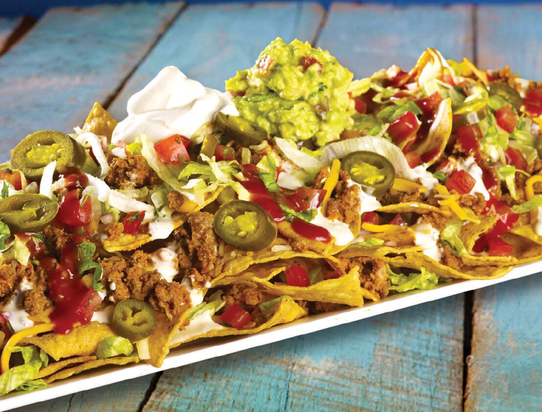 Des nachos garnis de viande, de fromage, de piments jalapeño et de guacamole, servis sur une table en bois.
