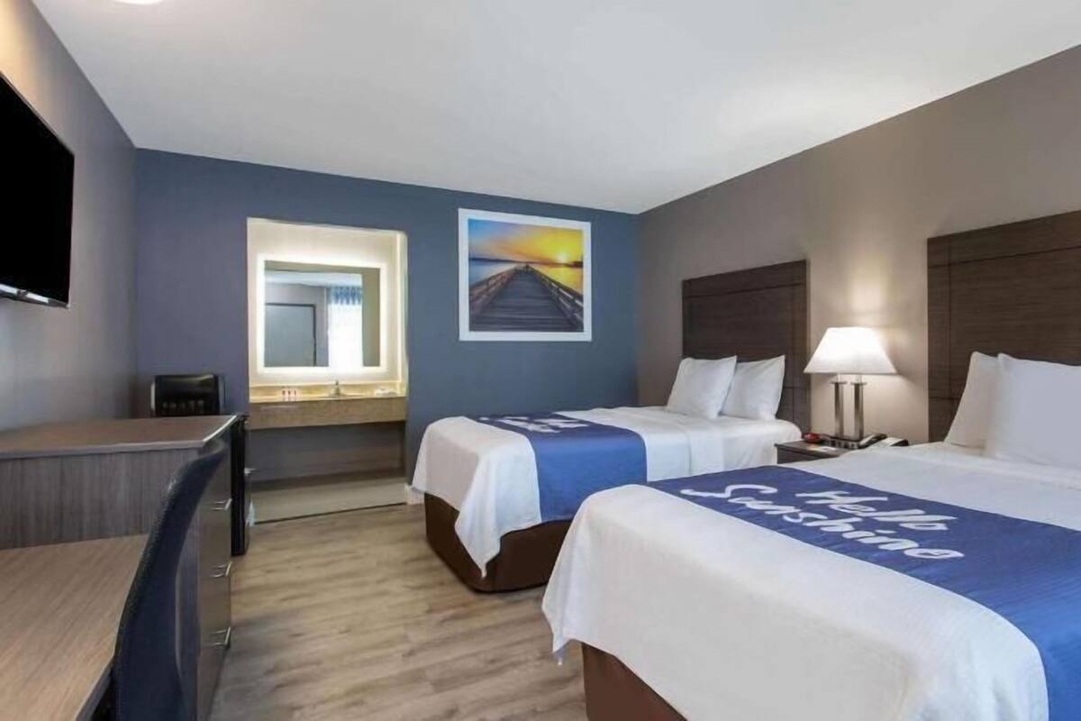 A hotel room with two beds, a desk, a chair, a TV, and a painting on the wall.