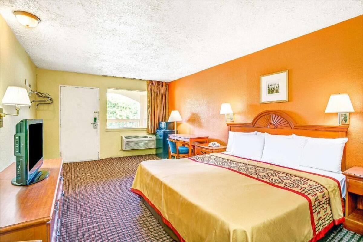 A hotel room with a bed, bedside lamps, a desk with a computer, a TV, and a window with curtains.