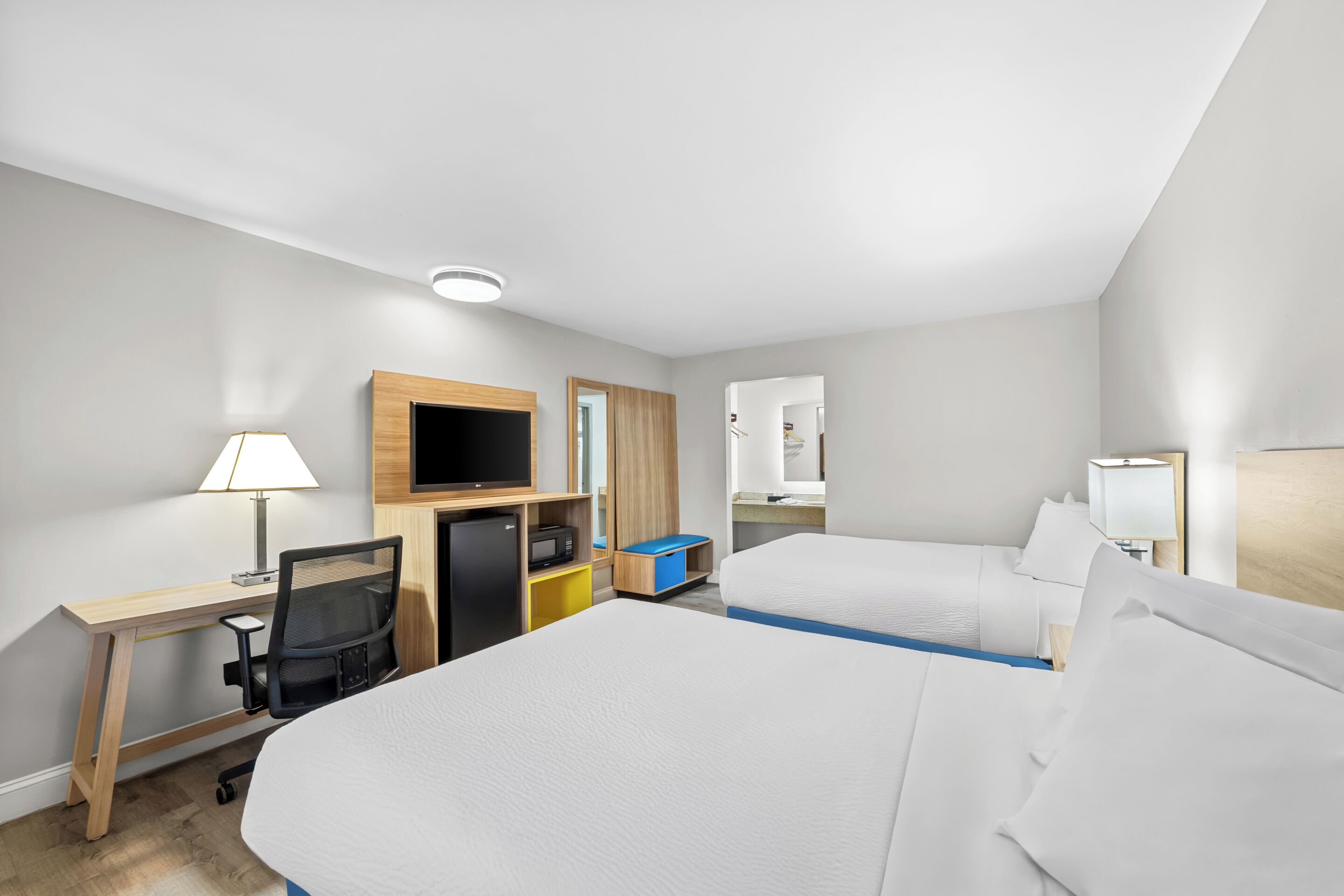 Een hotelkamer met twee bedden, een bureau met stoel, een televisie en een klein keukenblok.