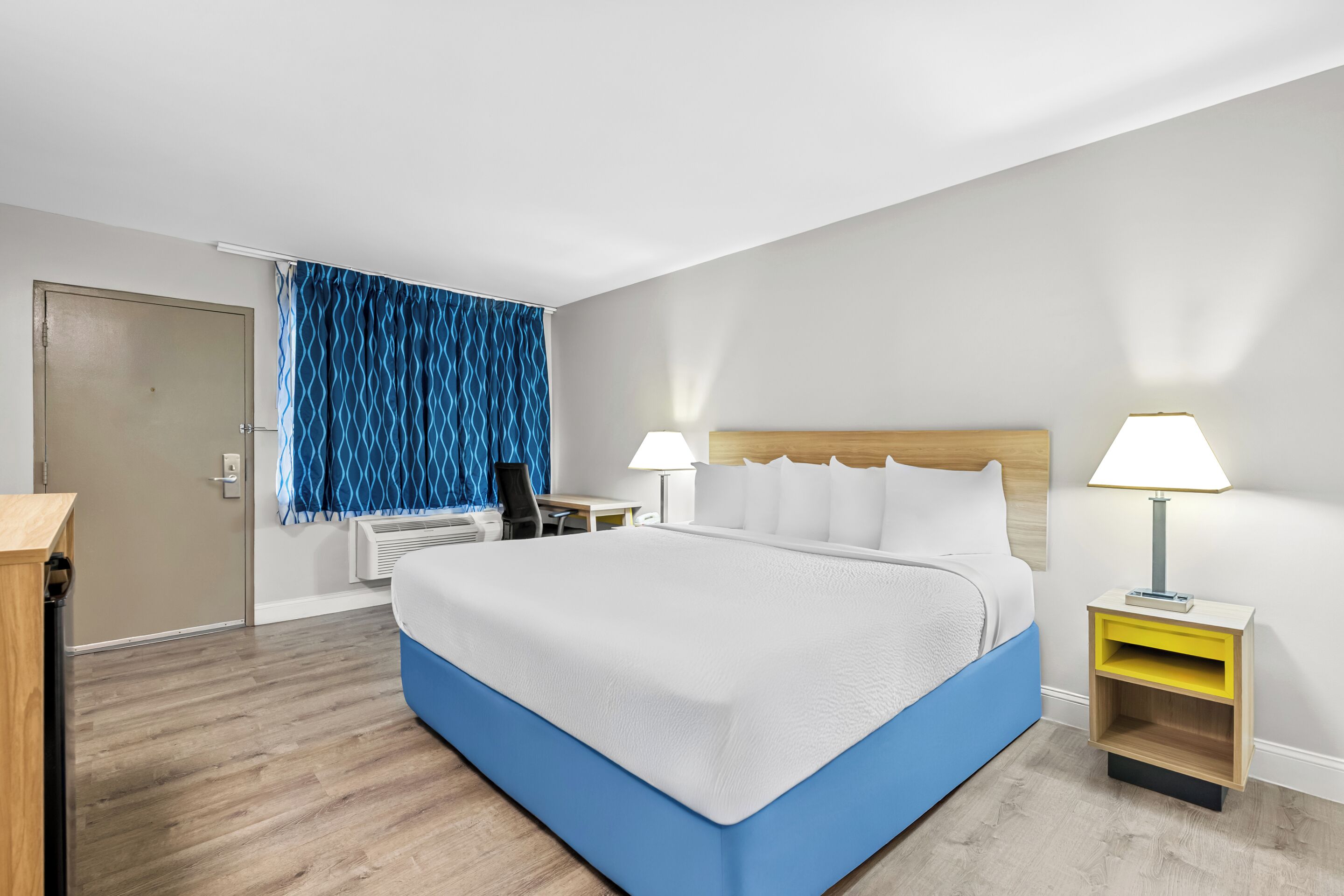 A hotel room with a large bed, two bedside tables with lamps, a desk, and a chair.