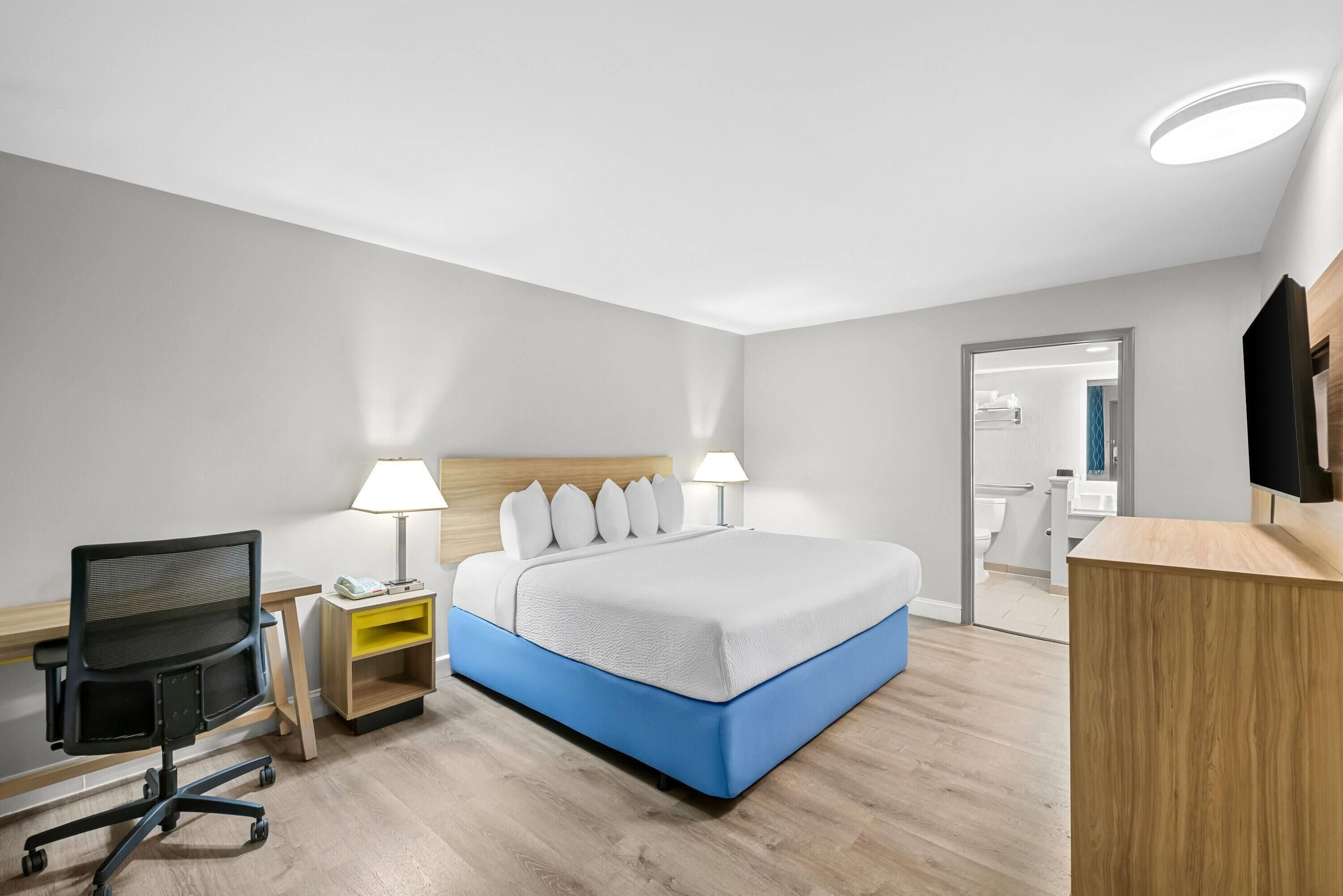 A modern hotel room with a bed, desk, chair, lamp, and a TV.
