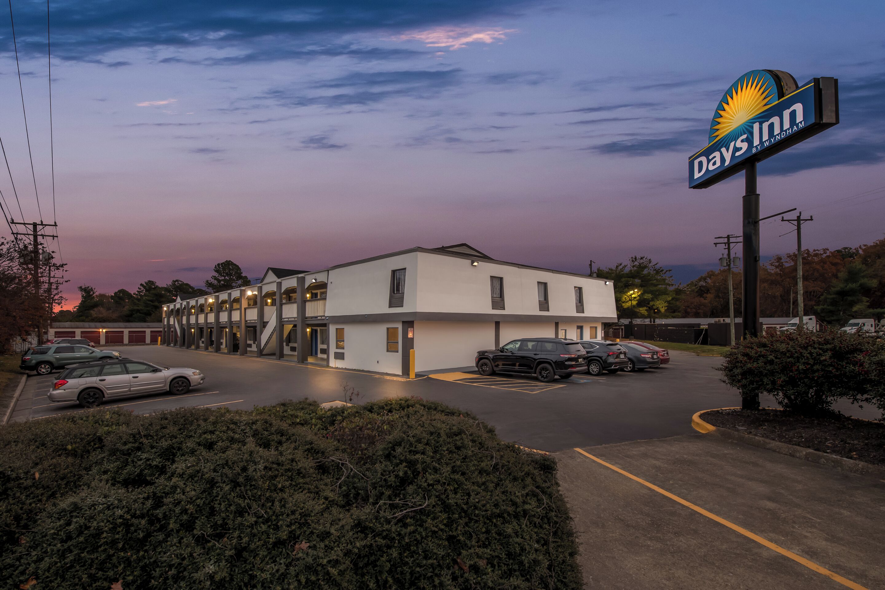 Um motel Days Inn com estacionamento, vários edifícios e céu ao pôr do sol.