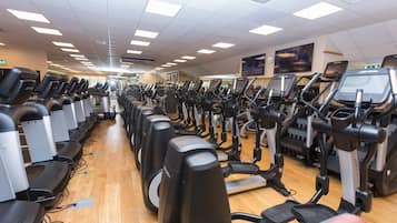 Un gimnasio con múltiples cintas de correr y bicicletas estáticas dispuestas en filas.