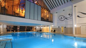 An indoor swimming pool with clear water, surrounded by a modern architectural design with glass walls and a high ceiling.