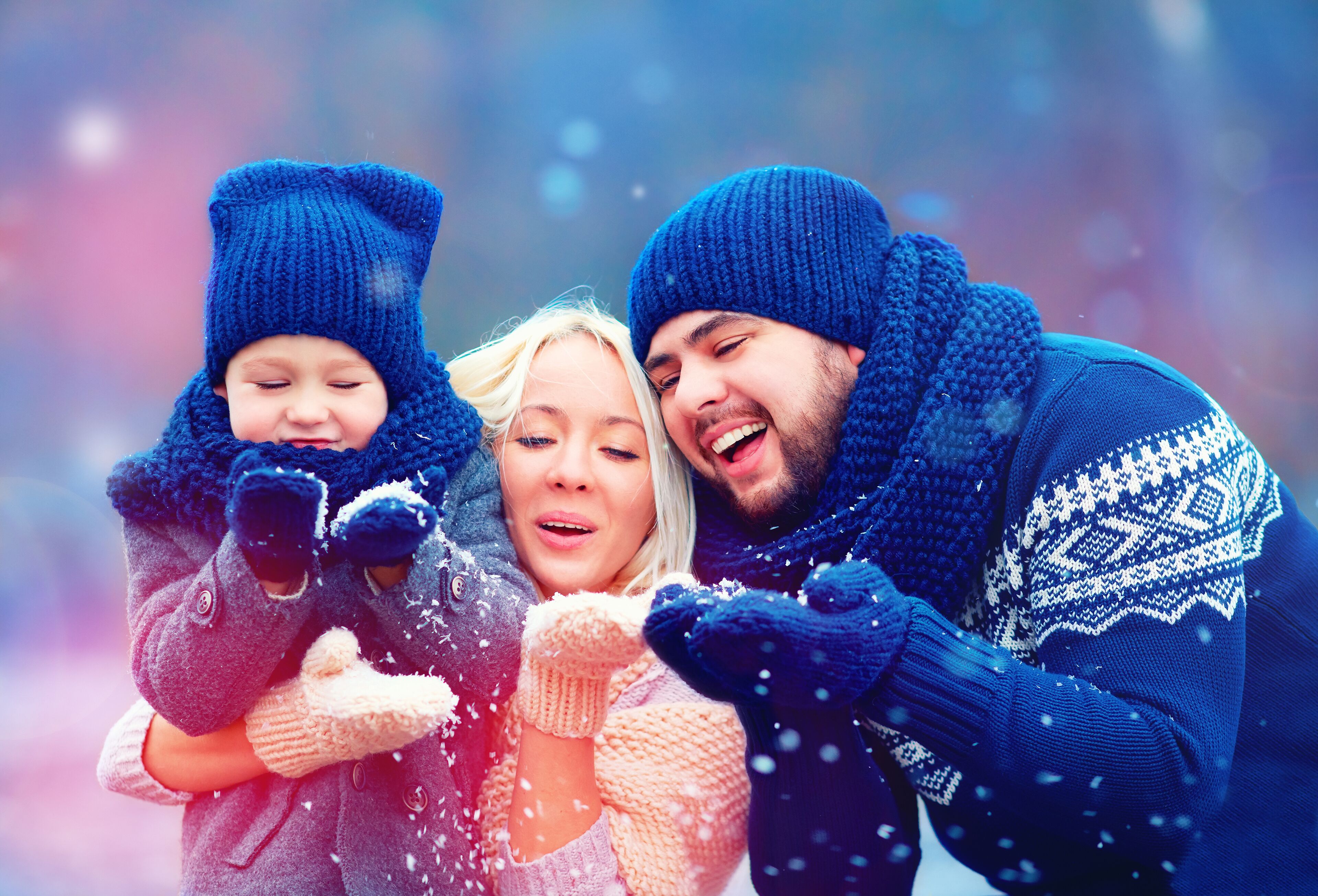 A family of three in winter clothing, with snowflakes visible in the air.
