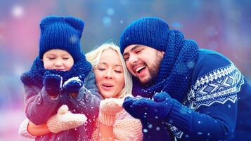 Una familia de tres personas vestidas para el invierno, con copos de nieve visibles en el ambiente.