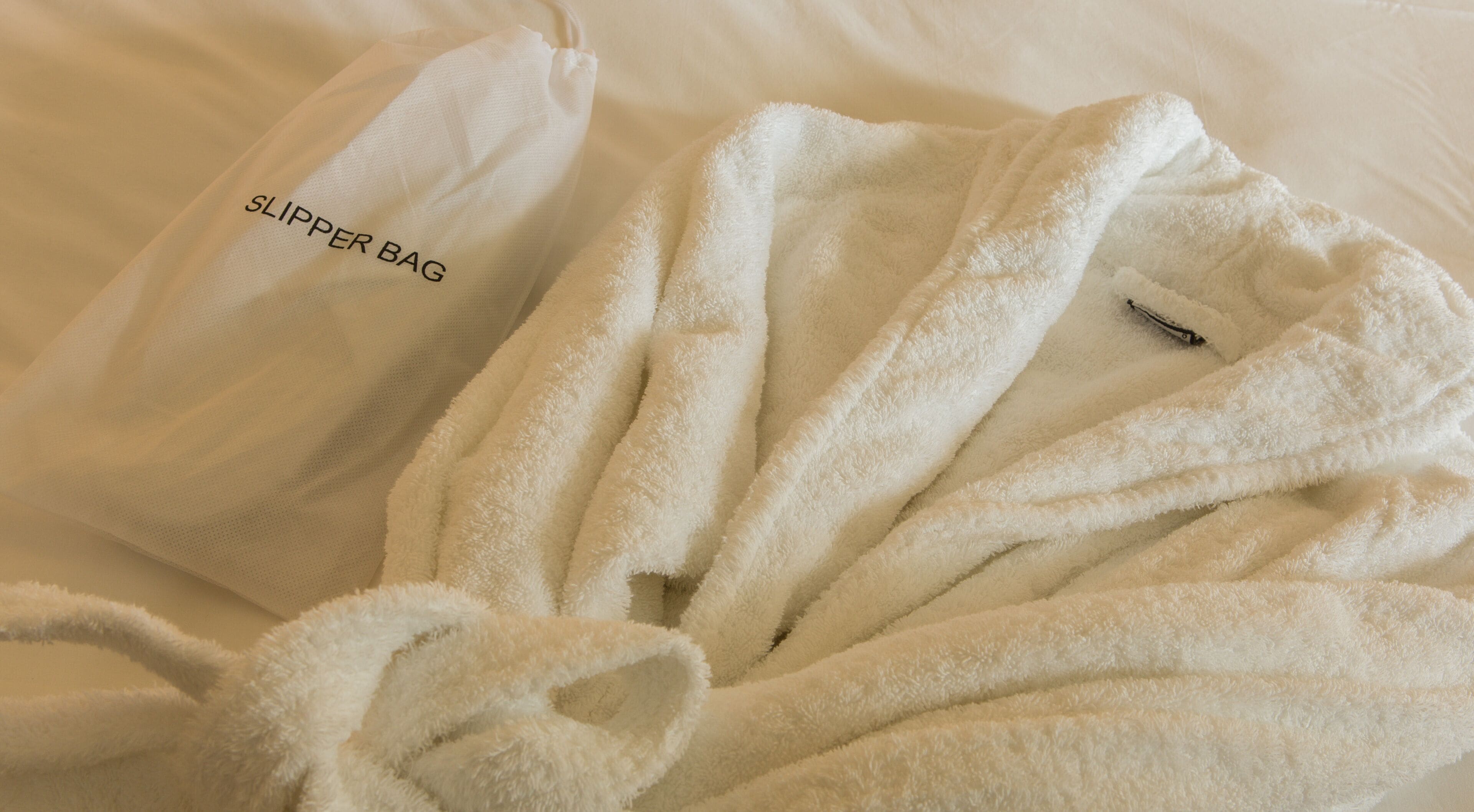 A white bathrobe and slippers on a bed.