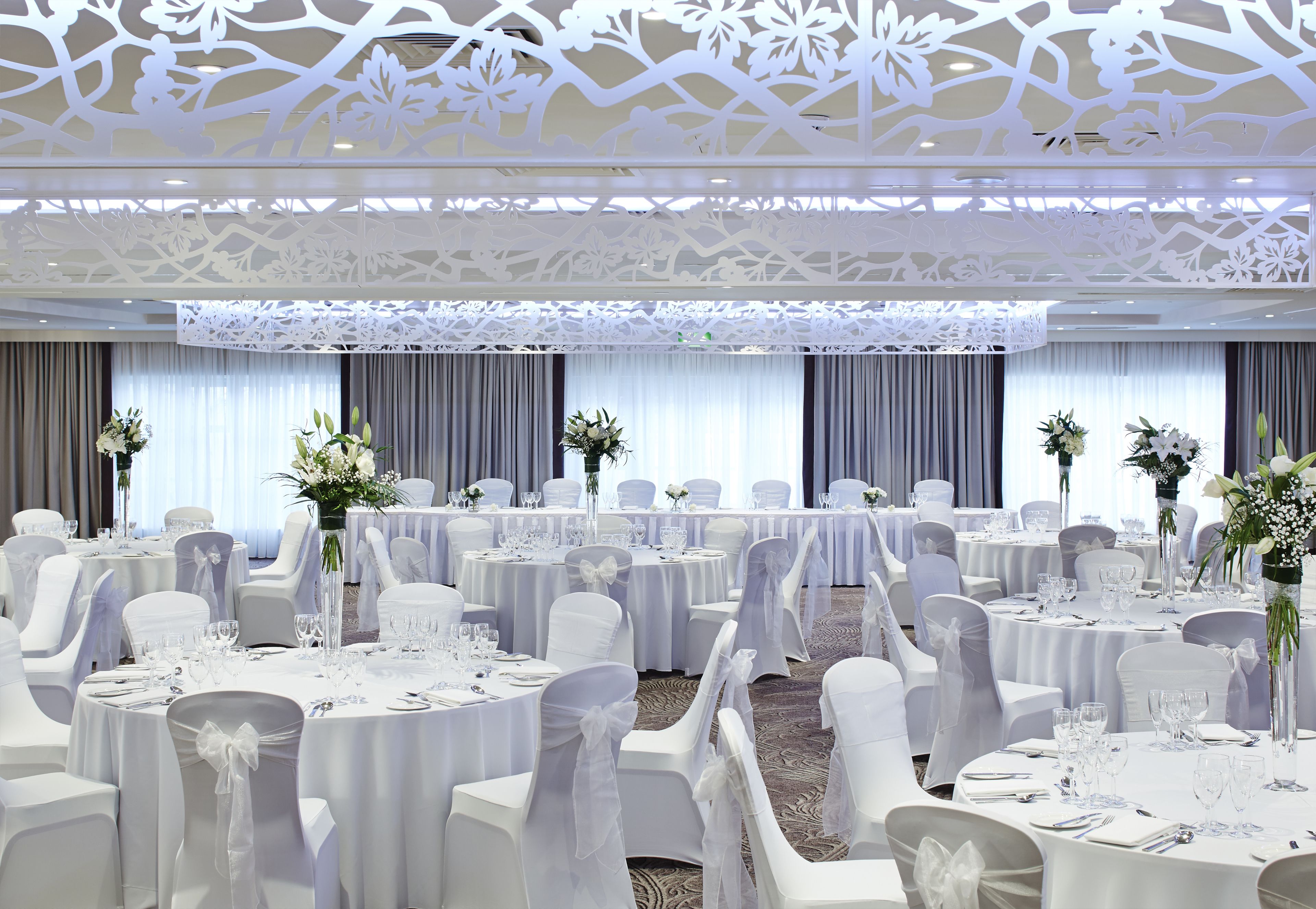 Un salón de banquetes con mesas redondas, manteles blancos y sillas con lazos blancos.