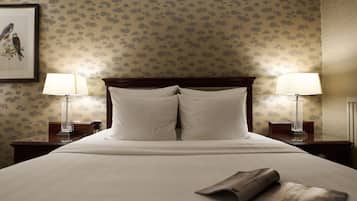 Una cama bien hecha con dos almohadas, un cuadro con pájaros en la pared y dos lámparas de noche.