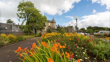 A historic building with a tower, surrounded by a garden with various flowers and a paved walkway.