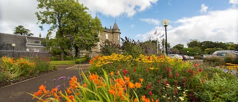Ein historisches Gebäude mit einem Turm, umgeben von einem Garten mit verschiedenen Blumen und einem gepflasterten Weg.