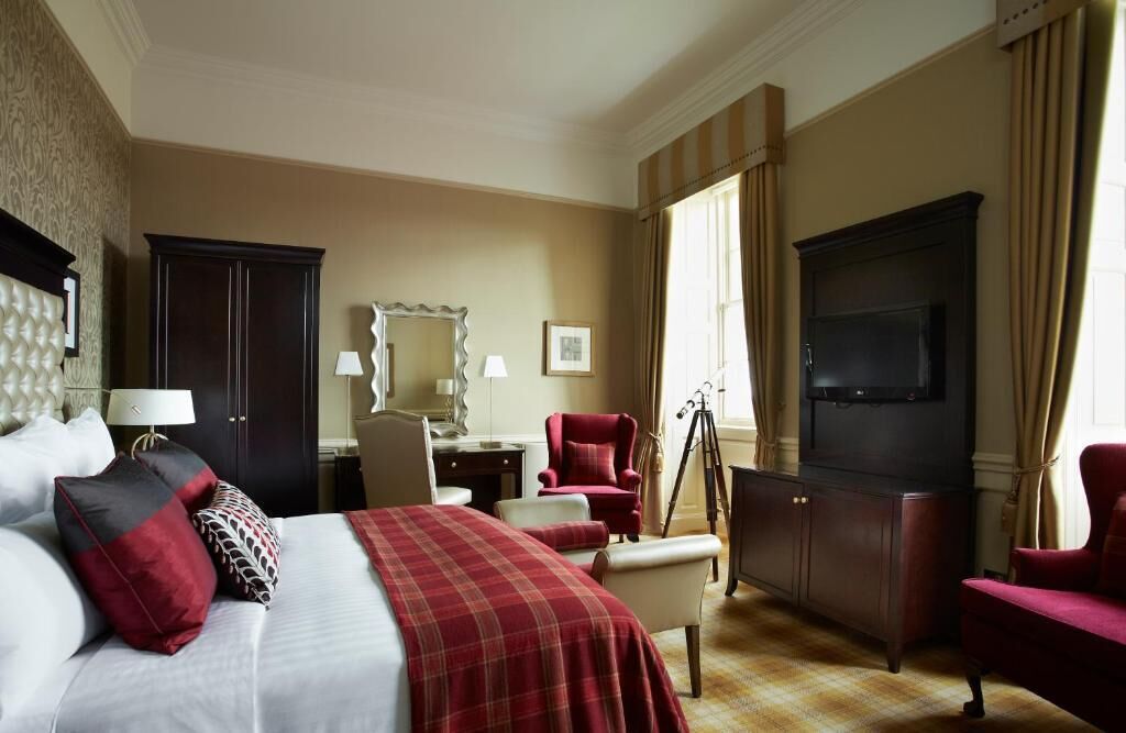 A hotel room with a bed, a desk, a chair, a television, and a wardrobe.