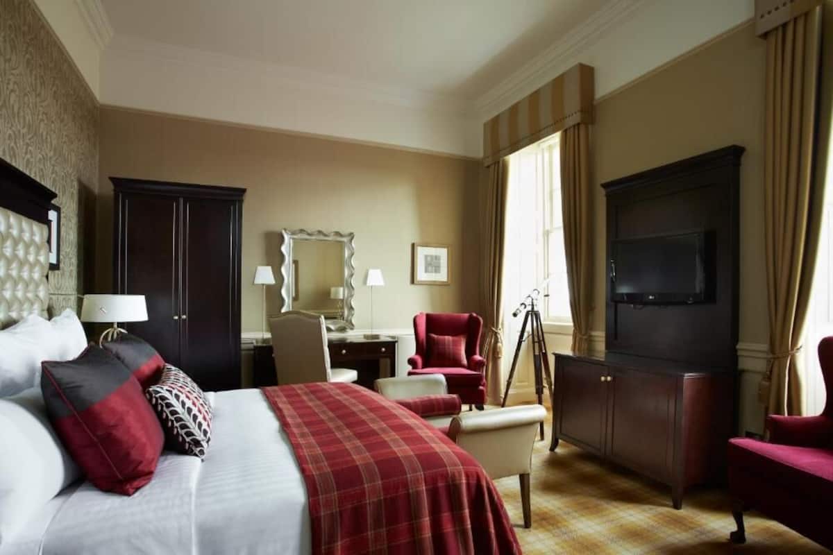 A hotel room with a bed, a desk, a chair, a television, and a wardrobe.