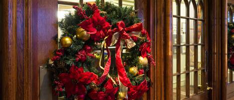 A wooden door with a large window, decorated with a Christmas wreath featuring red and gold ornaments.