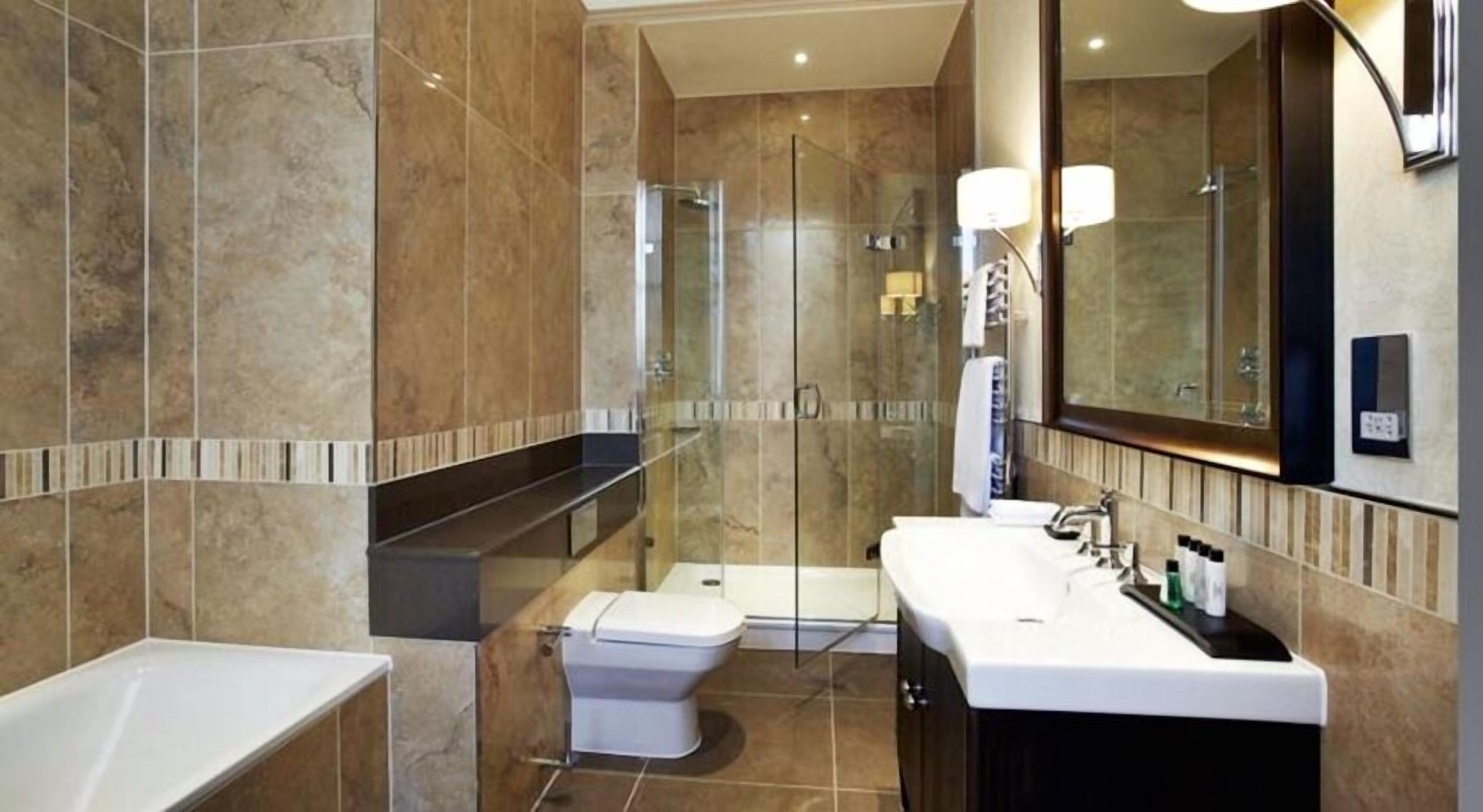 A modern bathroom with a glass shower enclosure, a toilet, a sink with a large mirror, and a bathtub.