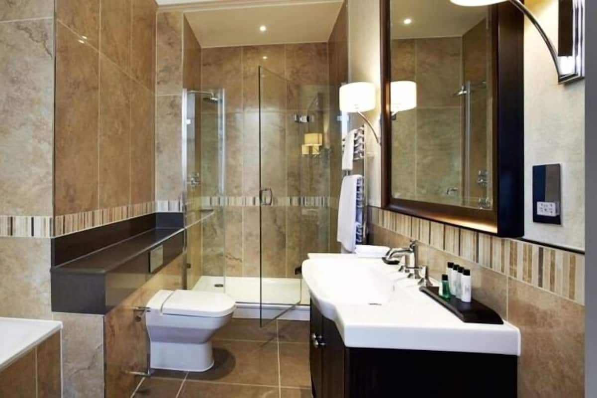 A modern bathroom with a glass shower enclosure, a toilet, a sink with a large mirror, and a bathtub.