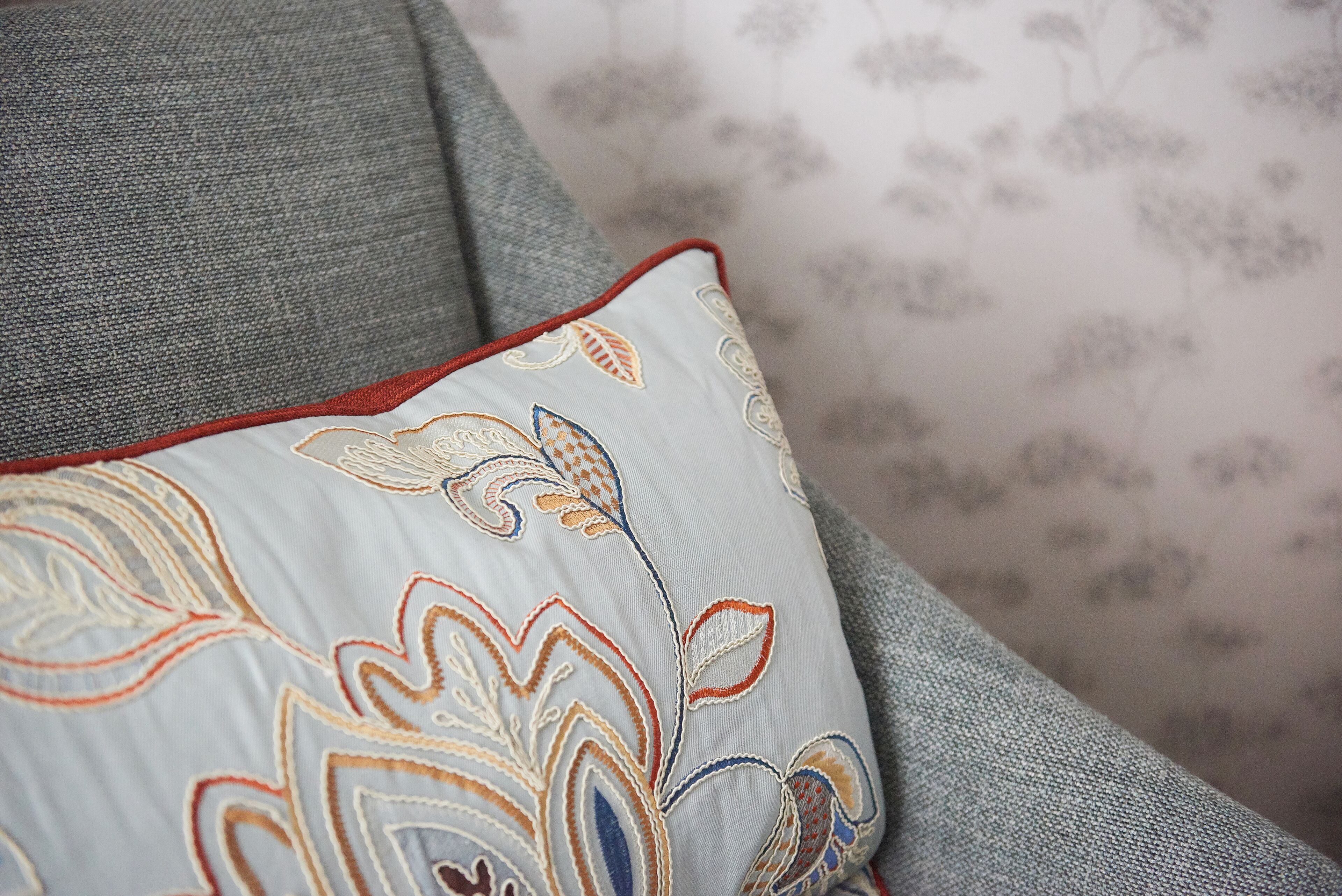 Et nærbillede af en grå sofa med en dekorativ pude med broderede blomstermønstre.