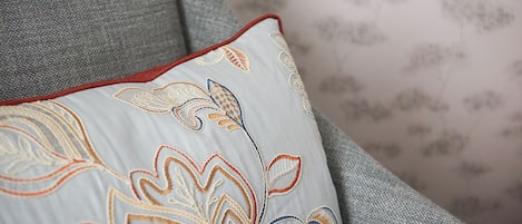 A close-up of a grey sofa with a decorative pillow featuring embroidered floral patterns.