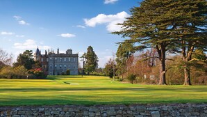 A large, historic building with a well-maintained lawn and trees in the foreground.