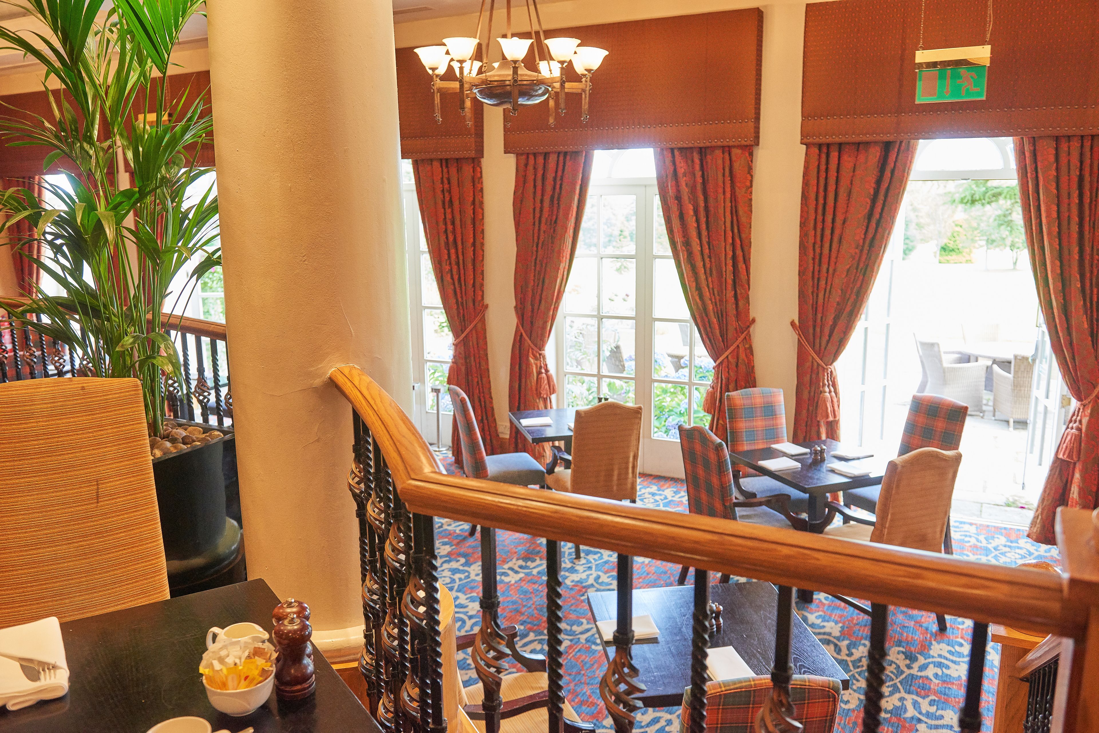A hotel lobby with a staircase, dining area, and large windows with curtains.