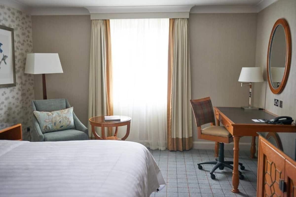 A hotel room with a bed, a desk, a chair, a round table, and a mirror.