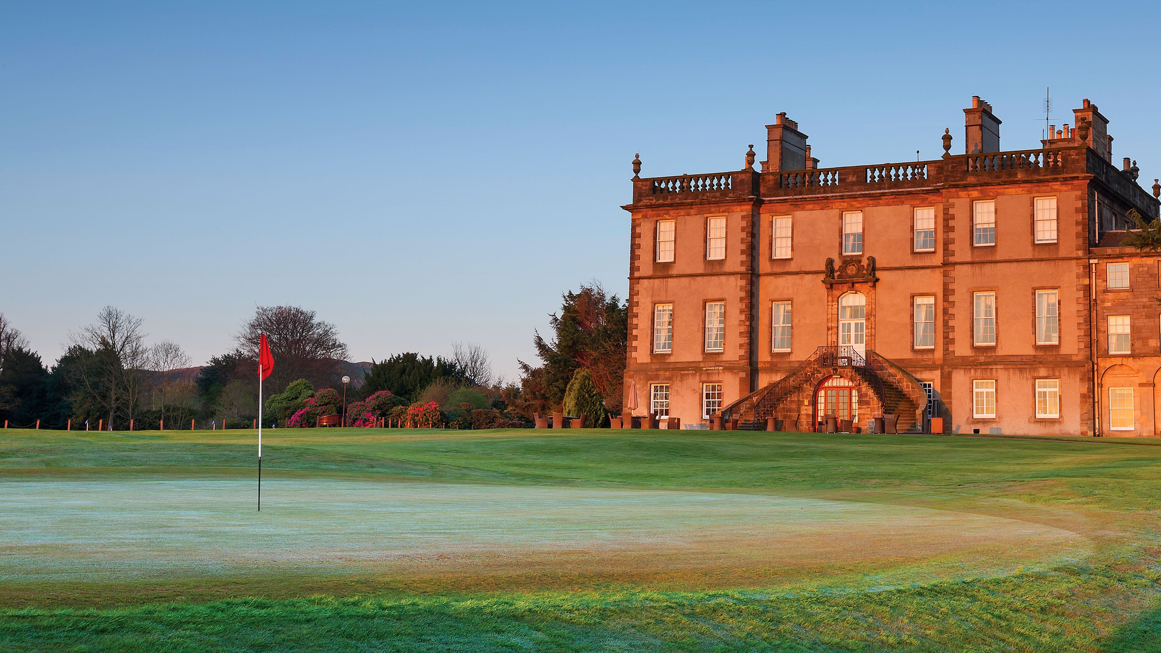 A large, historic building with a prominent entrance and a well-maintained lawn in front.