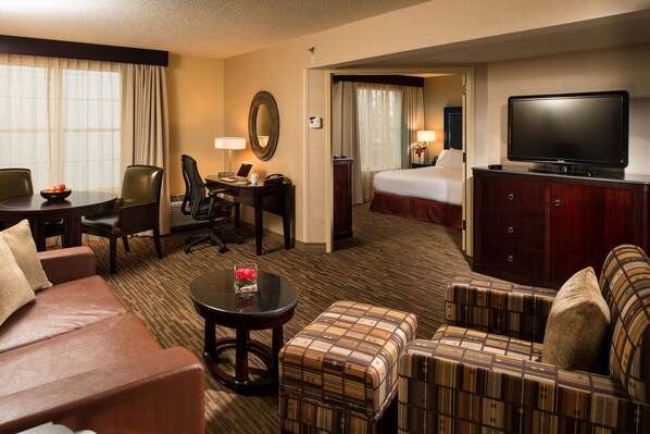 A hotel room with a bed, a TV, a desk with a chair, a sofa, and a small table with a vase. - DoubleTree Raleigh Durham Airport at Research Triangle Park (Durham)