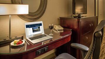 A hotel room with a desk, laptop, wine glass, and a telephone.