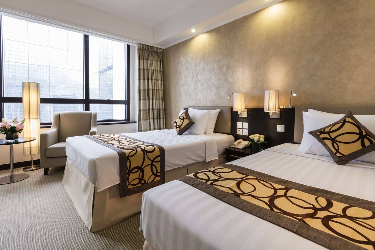 Ein Hotelzimmer mit zwei Betten, einem Sessel, einem Schreibtisch und einer Lampe.