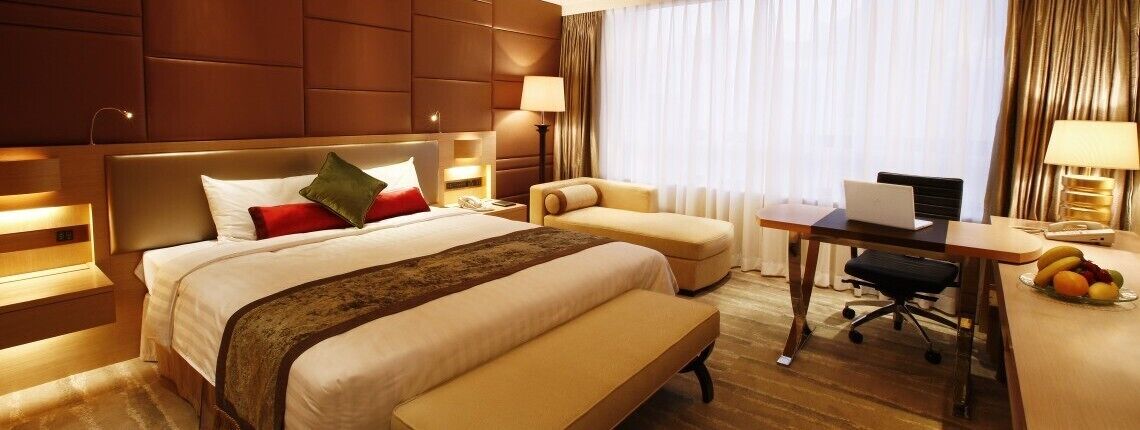 A hotel room with a large bed, a desk, a chair, and a laptop.