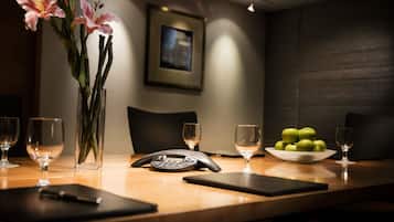 A conference table with a vase of flowers, a phone, a bowl of apples, and wine glasses.