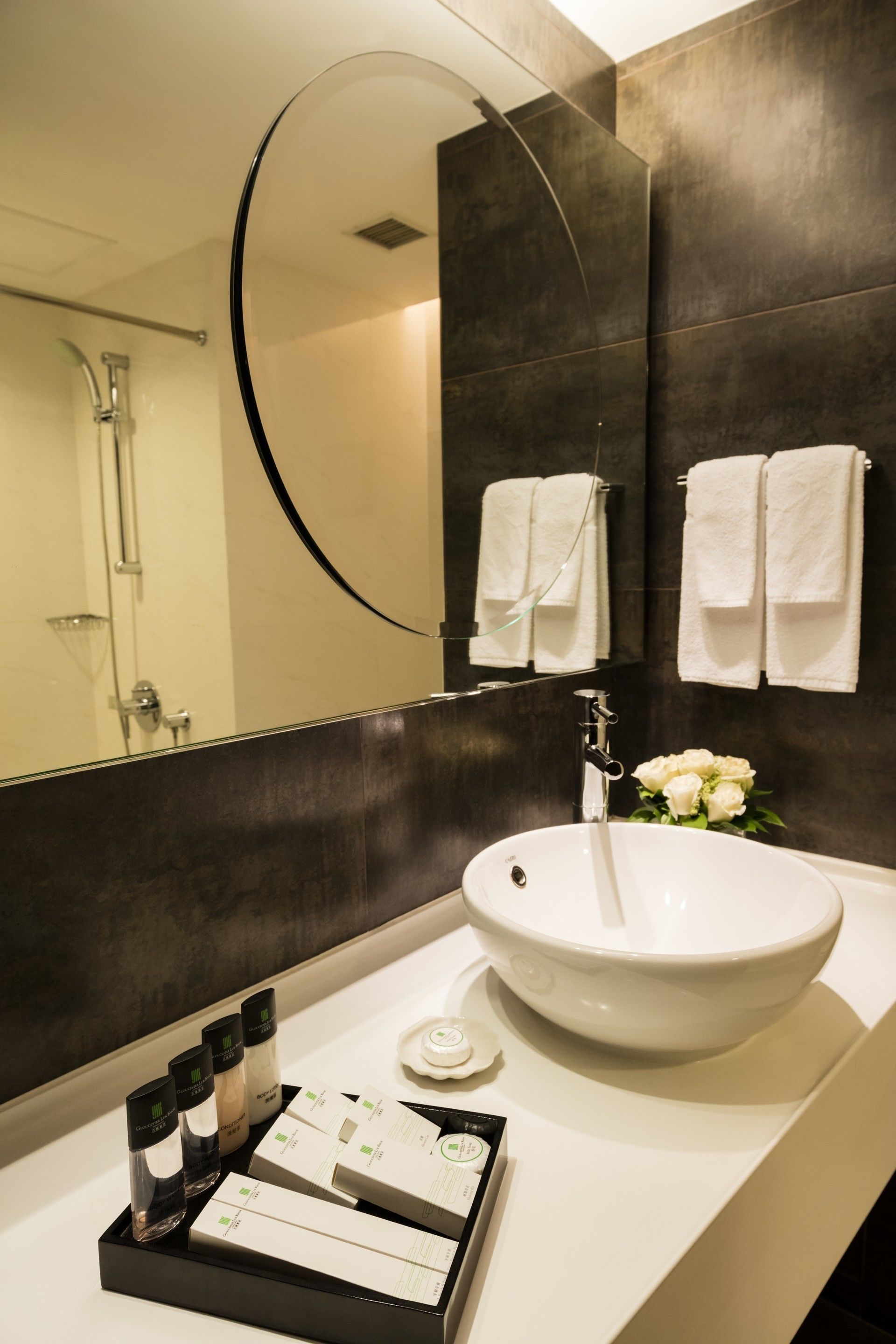A modern bathroom with a large mirror, a white sink, and a tray with toiletries.