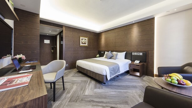 Une chambre d’hôtel moderne avec un grand lit, un bureau avec un ordinateur portable, une chaise et une table à manger avec des fruits.