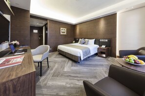 A modern hotel room with a large bed, a desk with a laptop, a chair, and a dining table with fruit. - Gloucester Luk Kwok Hong Kong (Hong Kong)