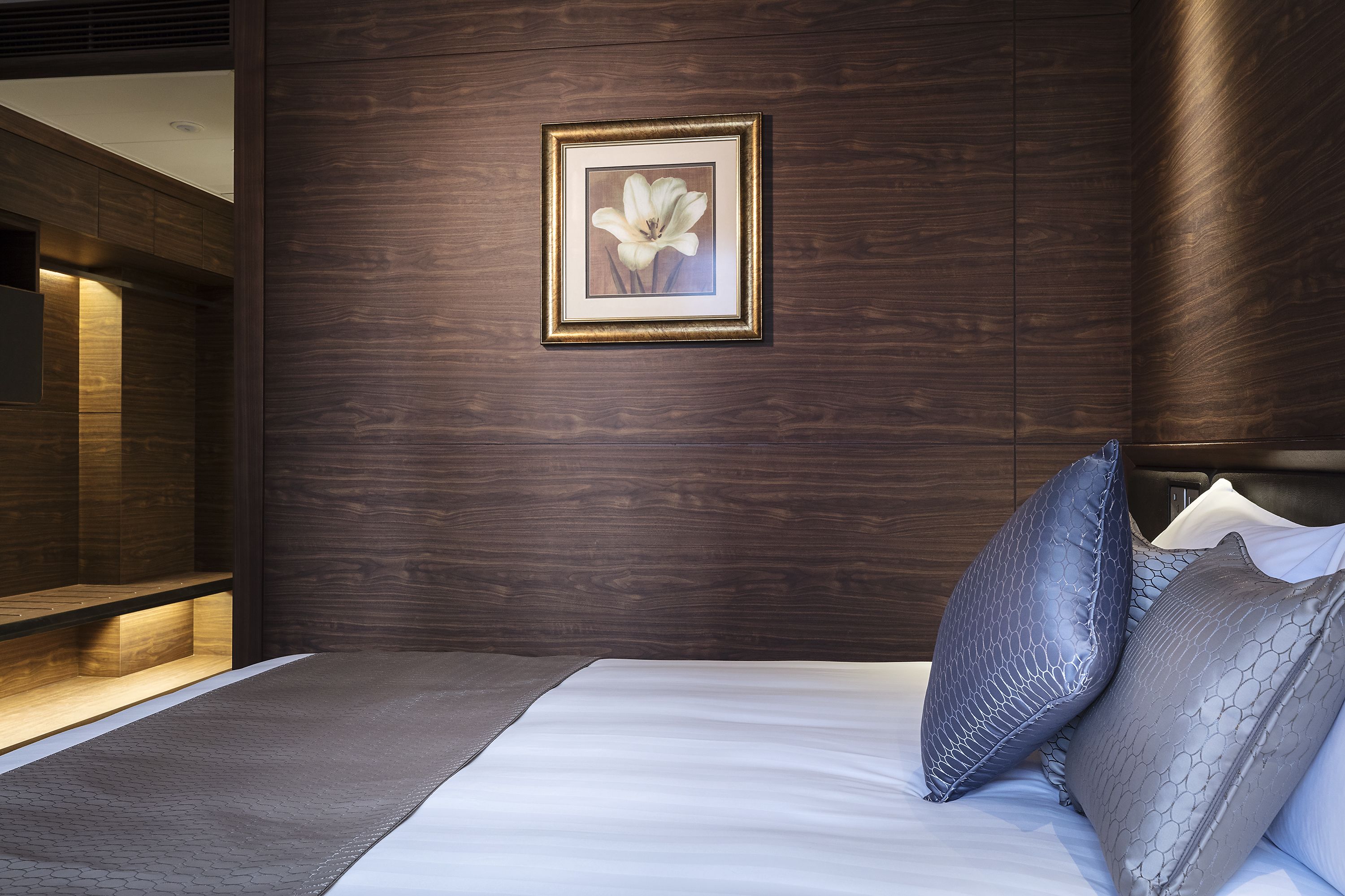 A modern bedroom with a wooden wall, a framed picture, and a bed with grey and white bedding.