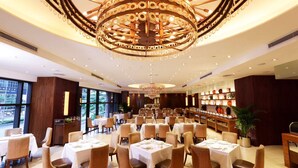 Un vaste espace dédié à la salle à manger, avec des tables rondes, des chaises confortables et un grand lustre décoratif.