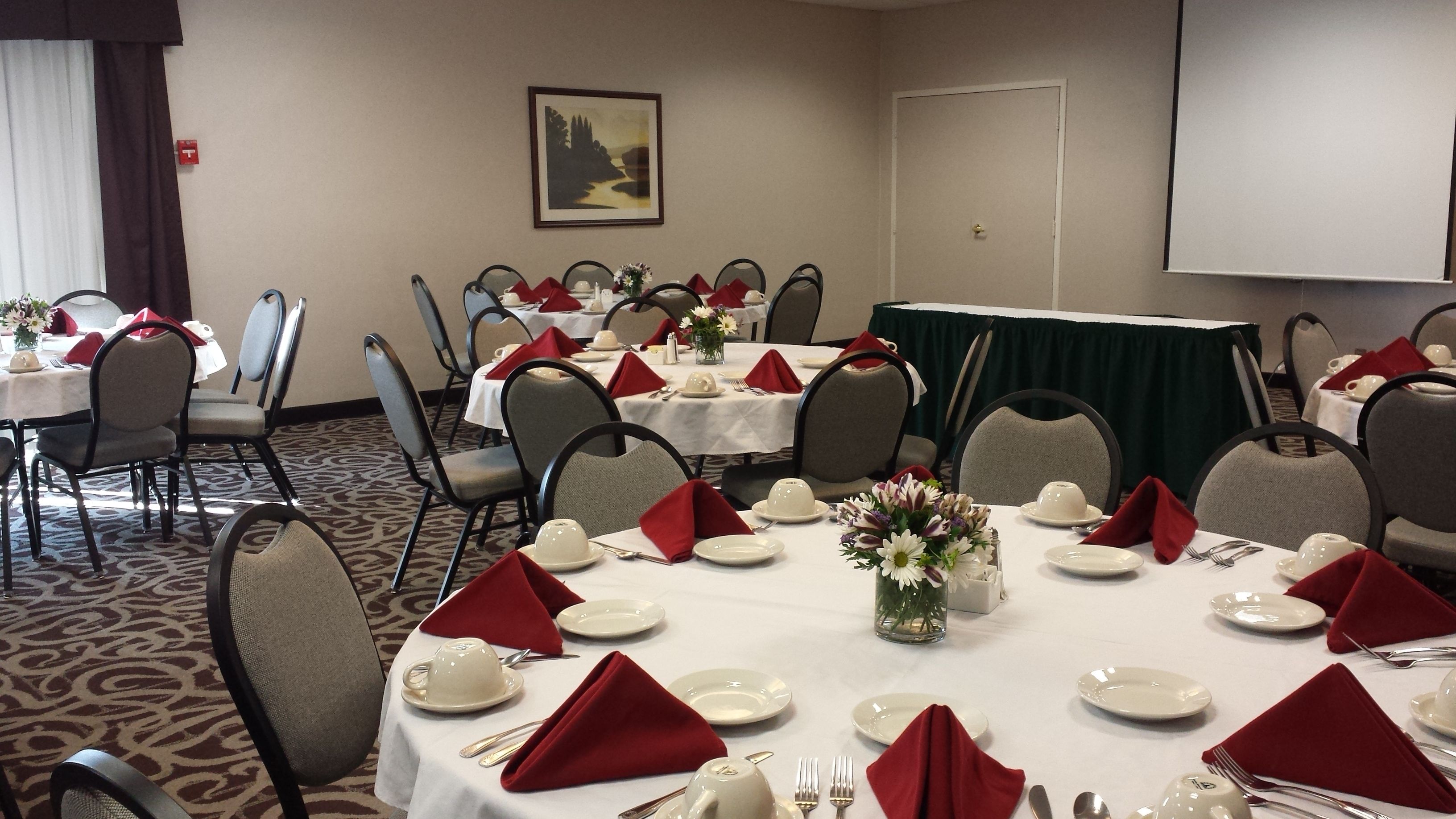 A conference room with round tables set for a meeting, equipped with chairs, plates, cutlery, and red napkins.