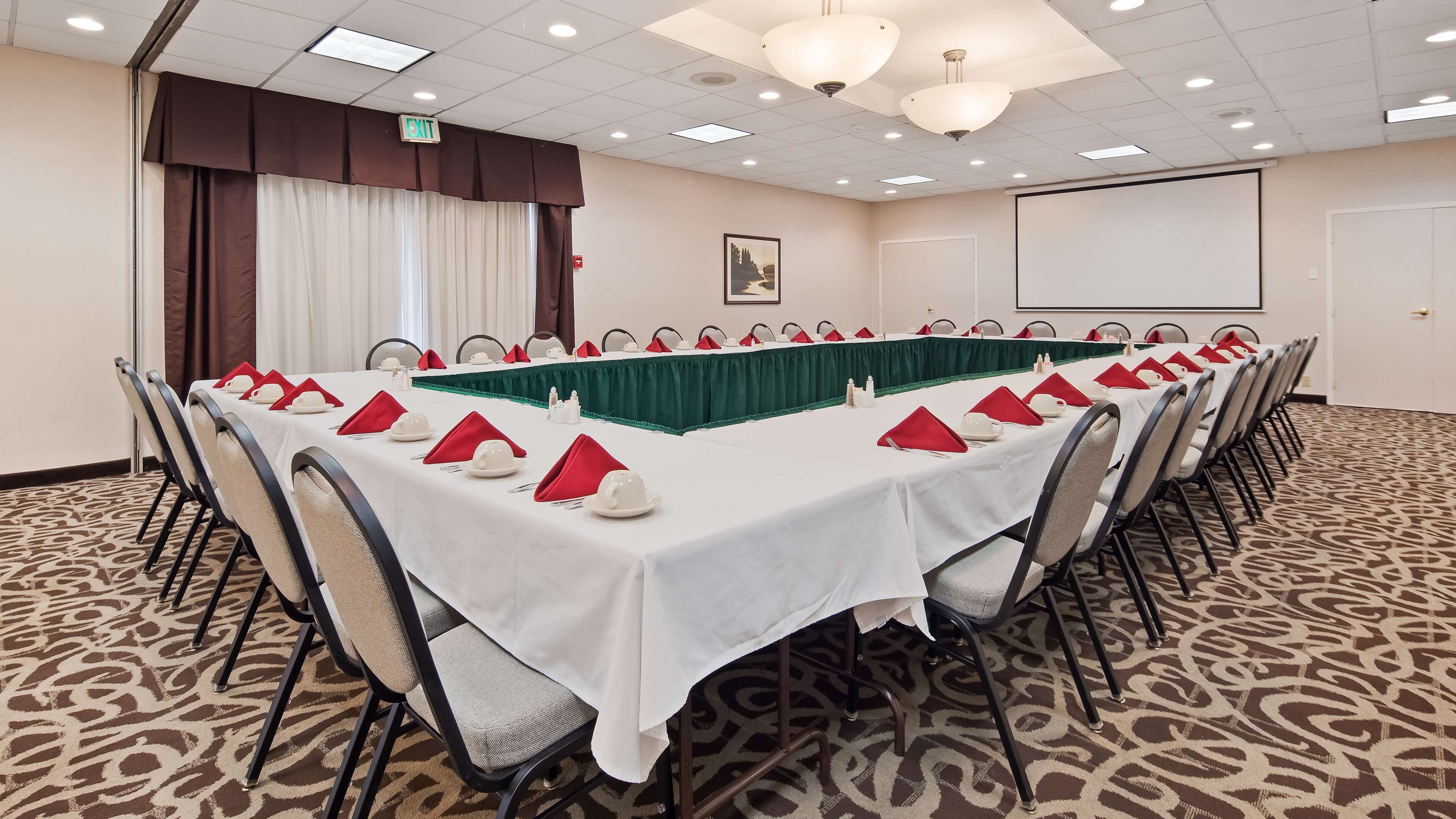 A conference room with a long table set for a meeting, equipped with chairs and a projector screen.