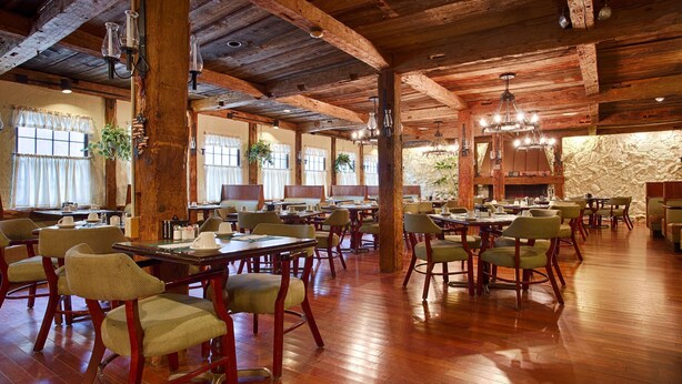 Un vaste espace dédié à la salle à manger, avec des tables et des chaises en bois, de grandes fenêtres et des luminaires suspendus.