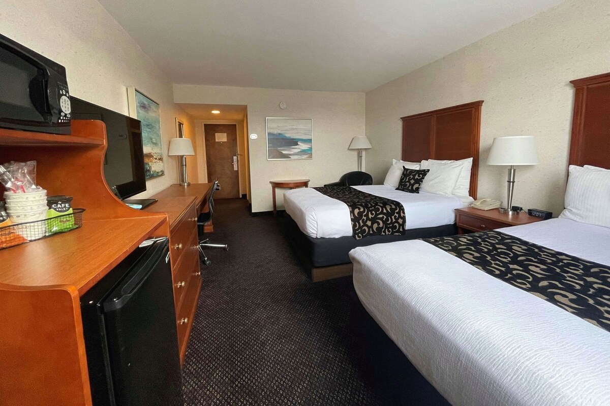 A hotel room with two beds, a desk, a television, and a view of the ocean.
