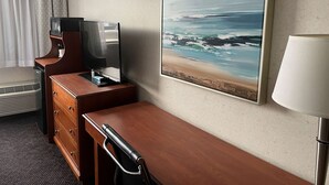 Une chambre d’hôtel avec un bureau en bois, un téléviseur à écran plat, un tableau représentant une scène de plage, une lampe et un radiateur.