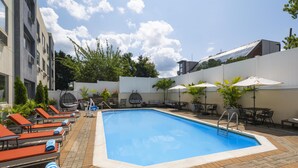 Piscina con sillones de descanso y sombrillas, rodeada de una cerca blanca y vegetación.