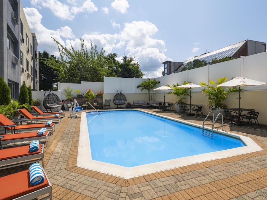 Ein Swimmingpool mit Liegestühlen und Sonnenschirmen, umgeben von einem weißen Zaun und Grünpflanzen.