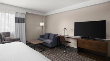 Habitación de hotel con cama, escritorio con televisor, silla, sofá y lámpara.