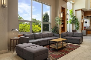 Een moderne woonkamer met een hoekbank, een salontafel en een groot raam met uitzicht op groen.