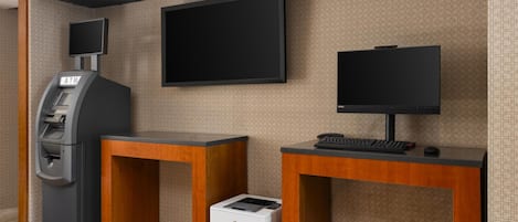 A reception area with a flat-screen TV, an ATM, a printer, and a keyboard on wooden desks.