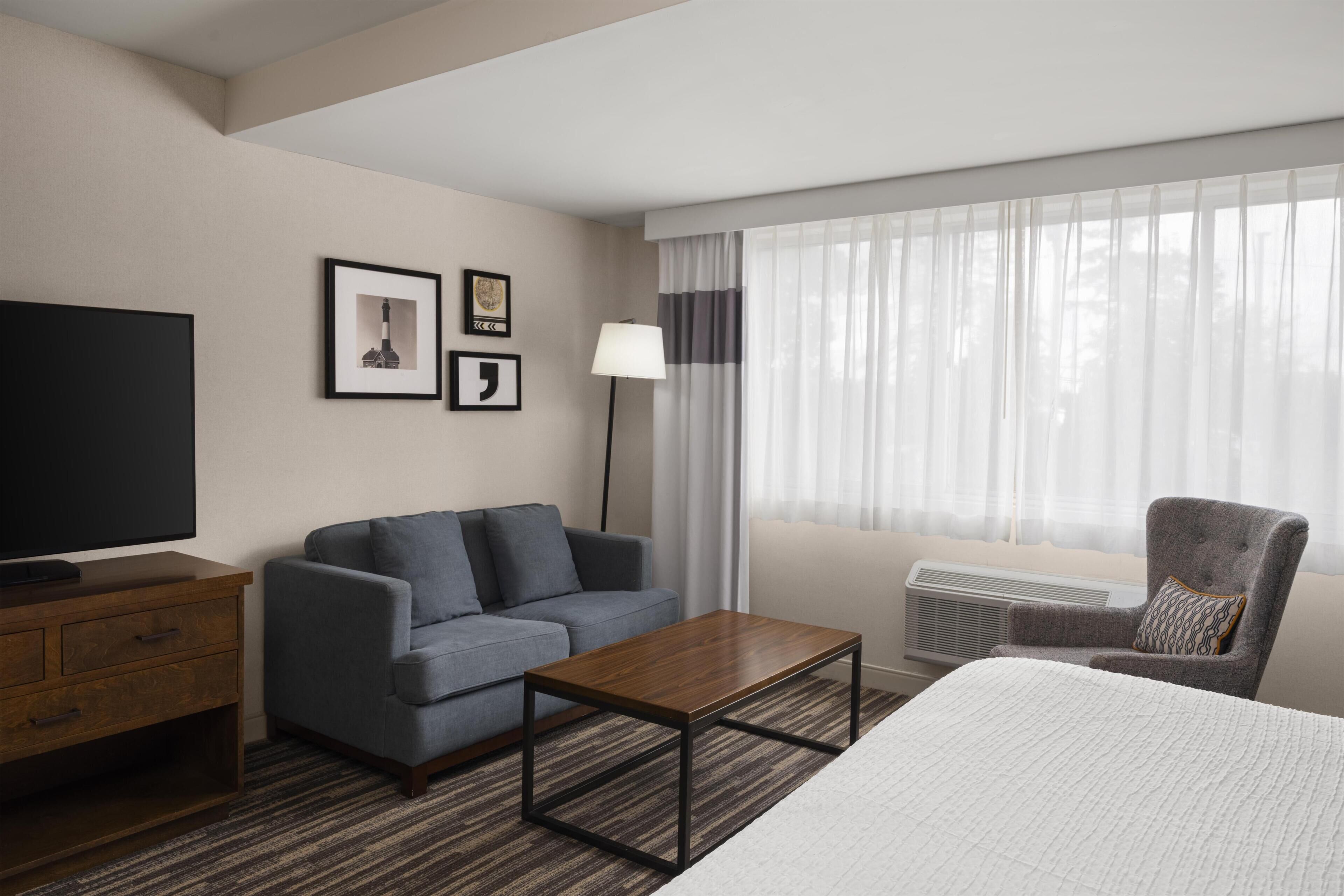 A hotel room with a bed, a sofa, a television, a desk, and a chair.