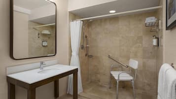 Une salle de bain moderne avec un lavabo blanc, un grand miroir, une douche avec une porte en verre et une chaise blanche.
